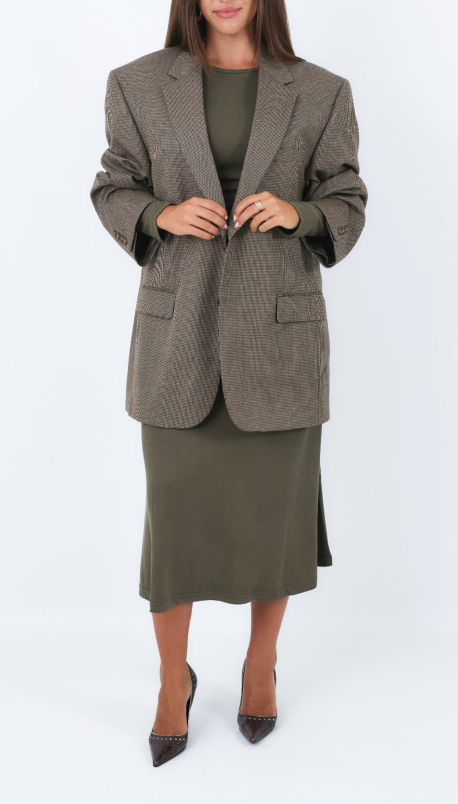 Woman wearing a brown houndstooth blazer and green skirt on a white background