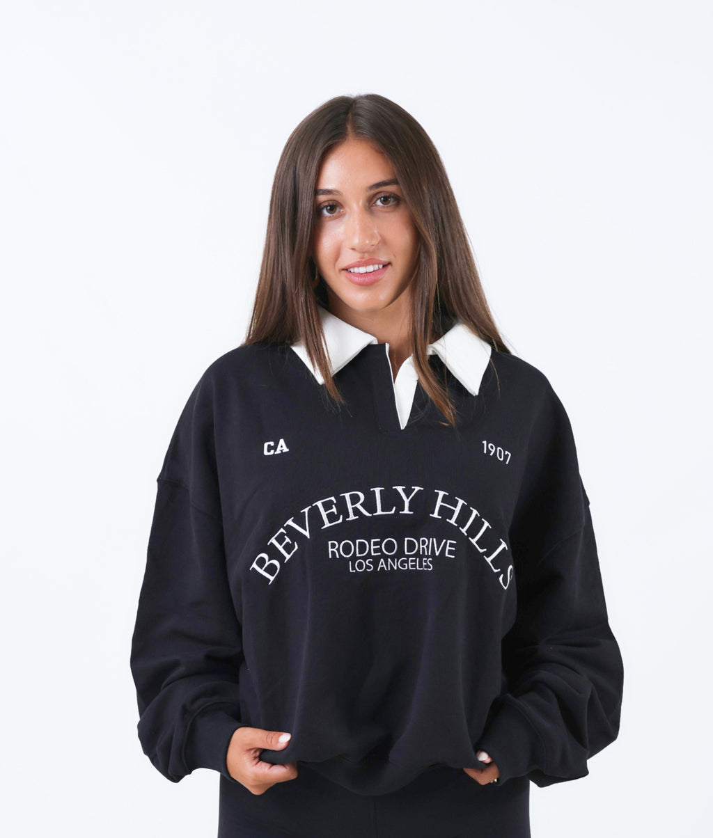Woman wearing a black 'Beverly Hills' sweatshirt with a white collar on a white background