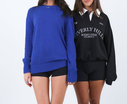 Two women wearing blue and black sweaters with visible branding on a white background