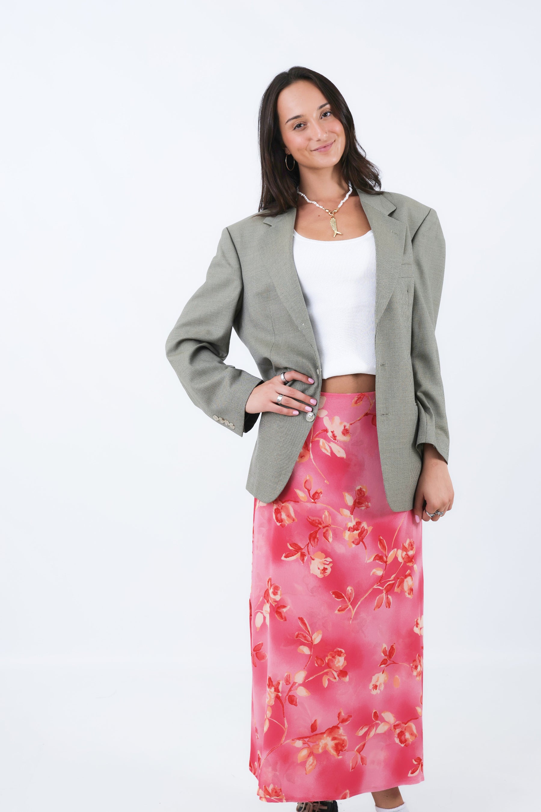 Woman wearing a gray blazer and pink floral skirt on a white background