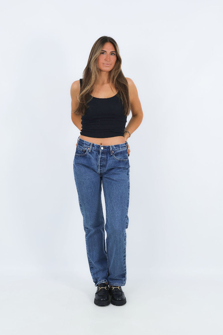 Woman wearing a black tank top and blue jeans on a white background